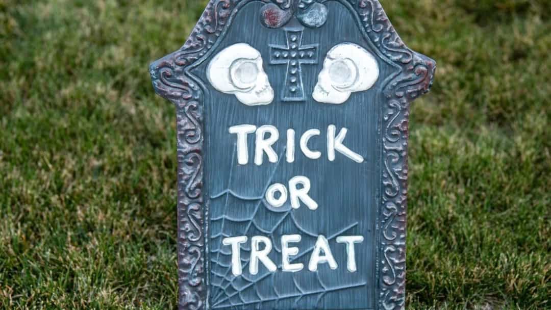 Çimlerin üzerinde, üzerinde “Trick or Treat” yazan dekoratif bir Cadılar Bayramı tabelası.