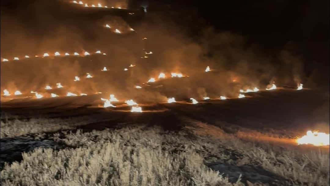 Gece saatlerinde hasat edilmiş tarlada yanan anızların alevleri ve yükselen duman.