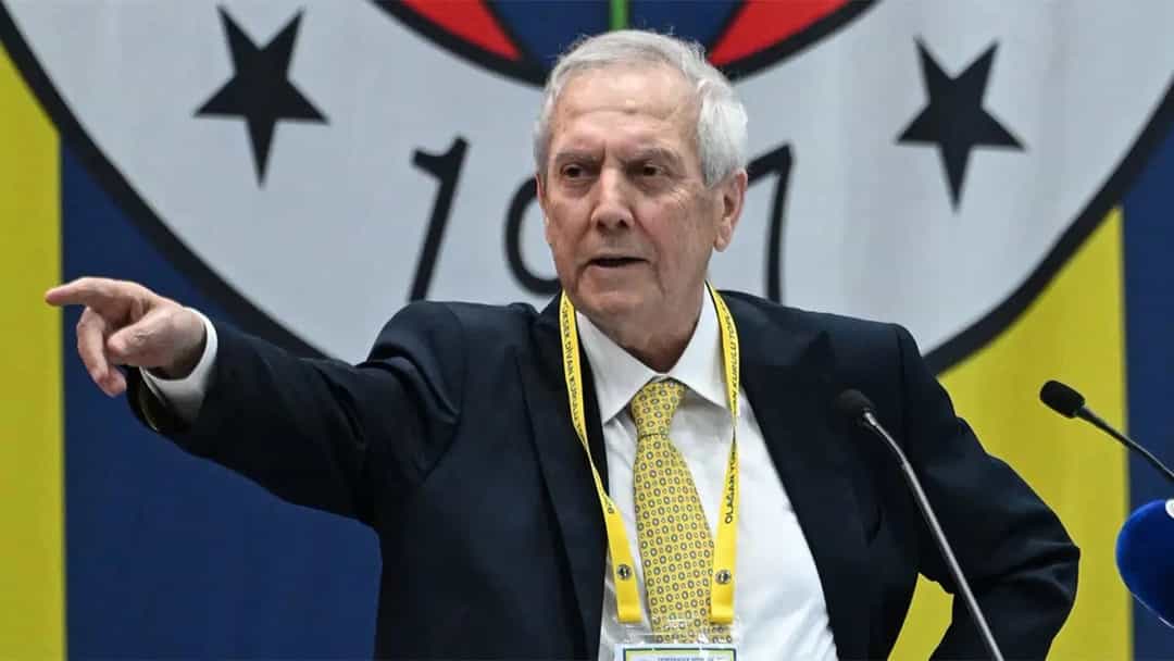 Aziz Yıldırım, Fenerbahçe amblemi önünde konuşurken eliyle işaret ediyor.