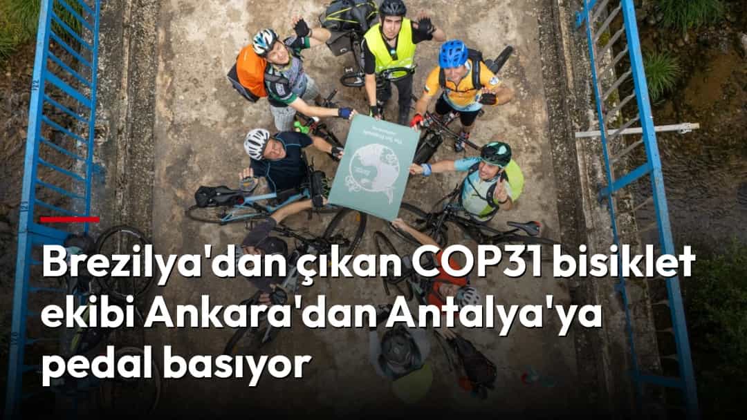 Bisikletçiler, bisikletleriyle birlikte bir bayrağın çevresinde toplanıyor.
