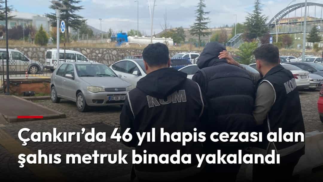 Kolluk görevlileri, kapüşonlu bir şüpheliyi araçların bulunduğu açık alanda eşlik ederek götürüyor.