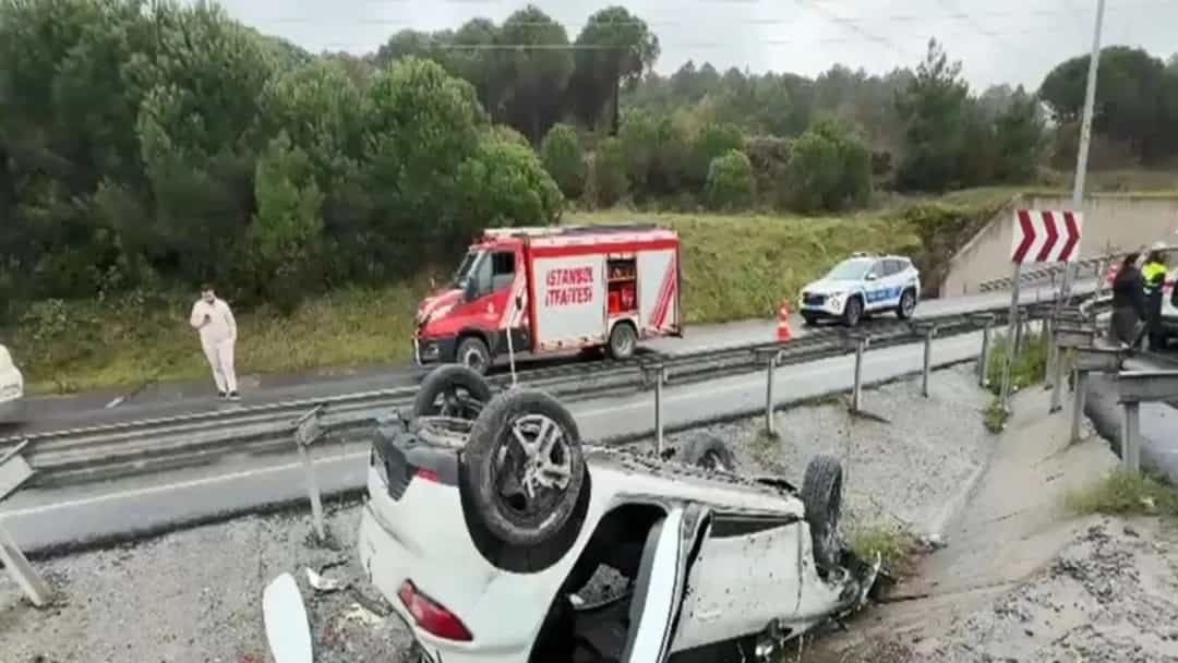 Yol kenarında takla atmış beyaz otomobilin çevresinde ekip araçları ve görevliler bulunuyor.