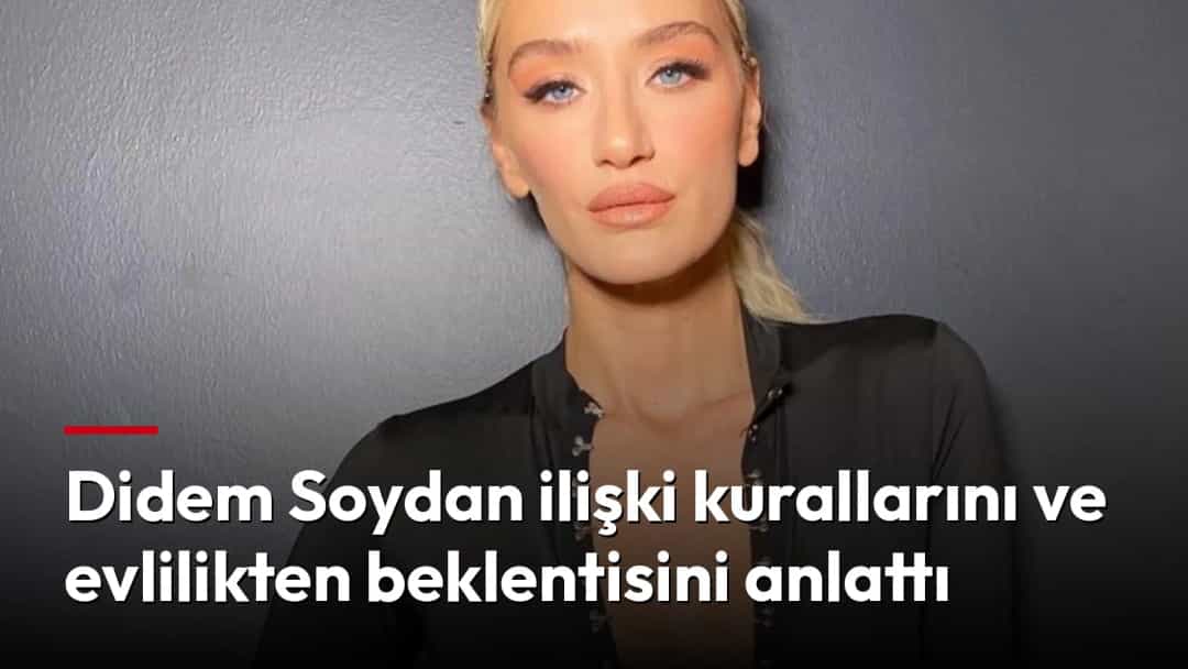 Didem Soydan siyah kıyafetiyle gri bir duvar önünde poz veriyor.