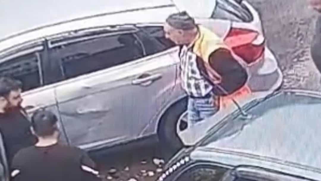 Güvenlik kamerası görüntüsünde park halindeki araçların yanında duran kişiler.