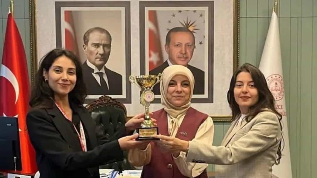 Üç kadın, bir kupa ödülünü birlikte tutarak fotoğraf çektiriyor.
