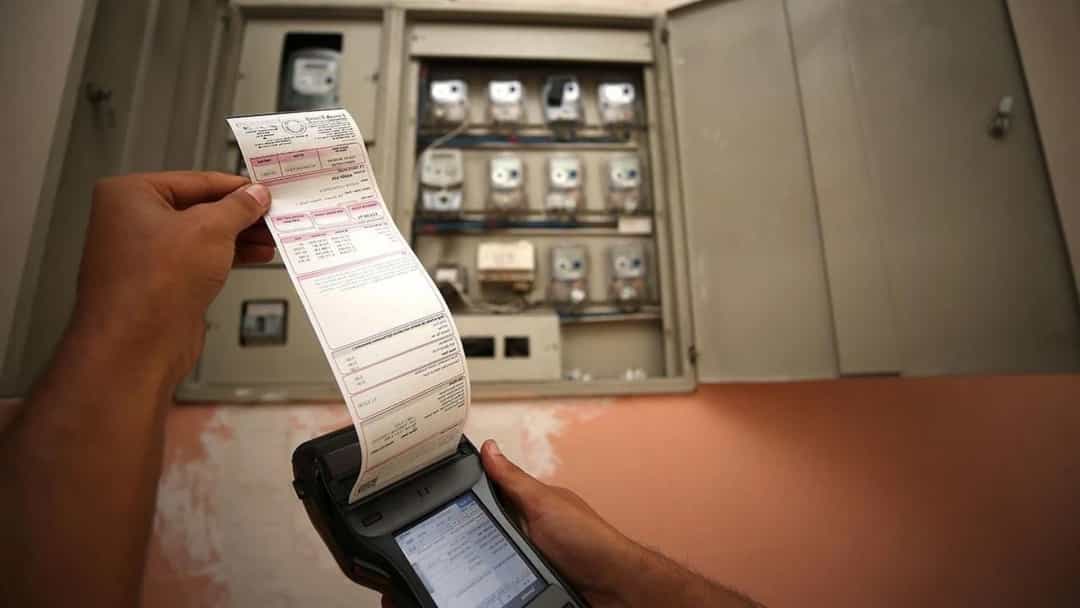 Elektrik sayaçlarının önünde elde tutulan elektrik faturası ve fiş yazıcısı.