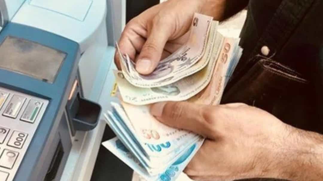 ATM yanında elindeki banknotları sayan bir kişi.