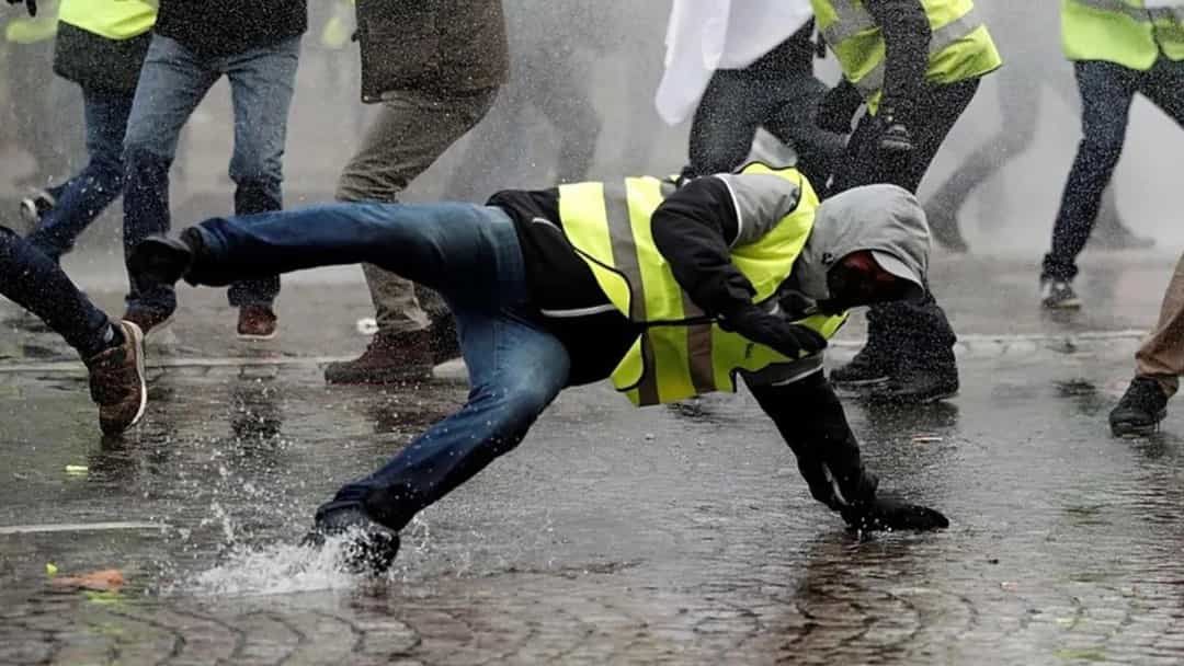 Fransa’da Sarı Yelekliler eyleminde, sarı yelekli bir protestocu yağmurlu ve ıslak sokakta yere doğru eğilirken çevresinde başka göstericiler görülüyor.