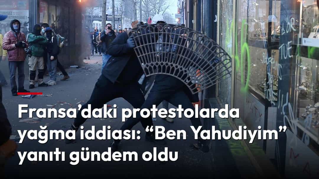 Fransa’daki protestolar sırasında göstericiler, duman ve alevlerin yükseldiği bir sokakta grafitili bir dükkânın önünde barikatı itiyor.