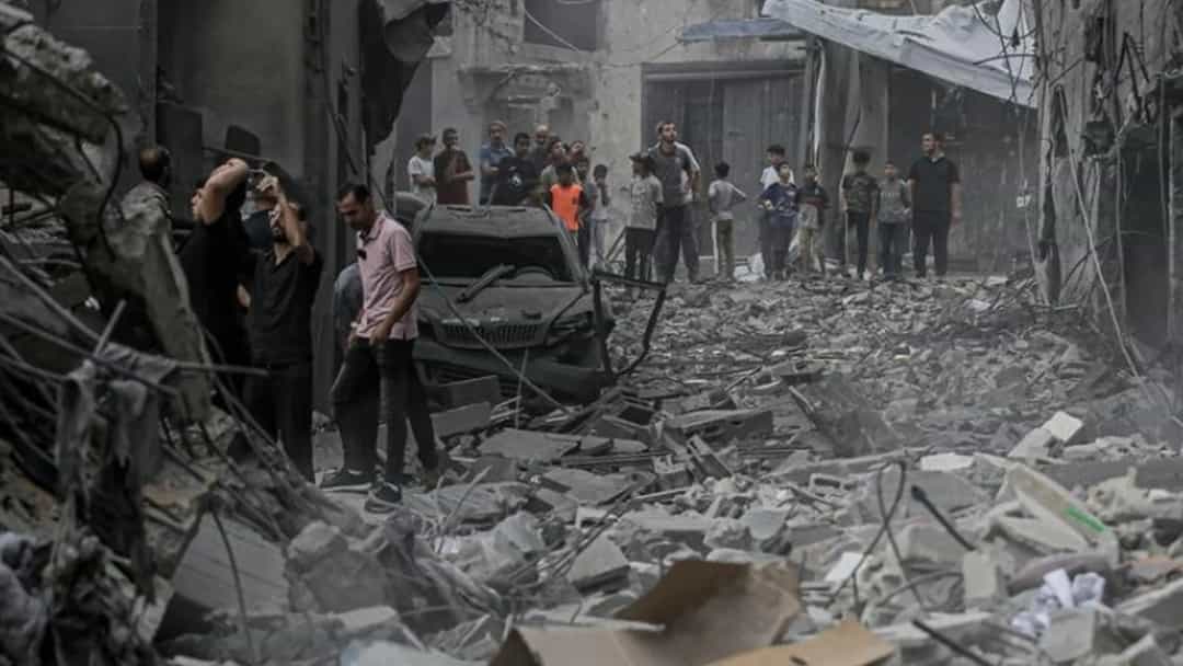 Gazze'de yıkılmış binaların arasında enkazla dolu bir sokakta duran insanlar