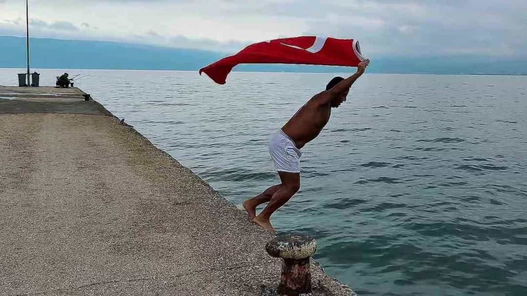 Bir kişi Türk bayrağını havaya kaldırarak kıyıdan denize giriyor.