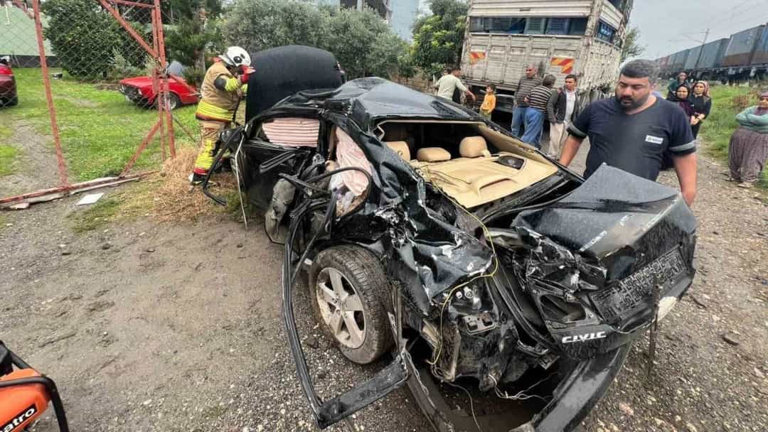 Tren yolu yakınında ağır hasar gören otomobilin çevresinde ekipler ve vatandaşlar bulunuyor.