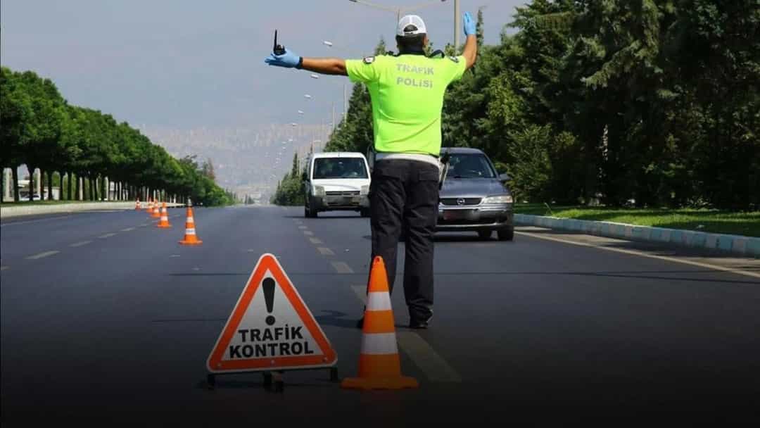 Trafik polisi, yolda koniler ve trafik kontrolü uyarı levhası önünde araçları yönlendiriyor.