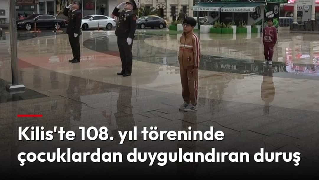 Yağmurlu bir meydanda tören sırasında askerlerin yanında saygı duruşunda duran çocuklar.