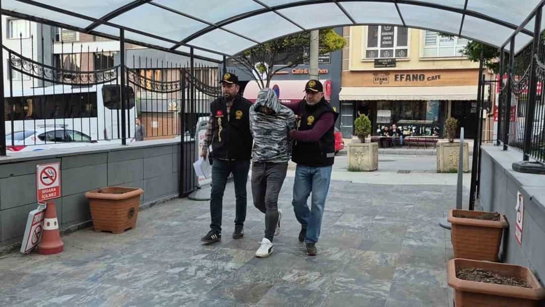 Polisler, yüzü kapalı bir kişiyi açık alanda yürütüyor.