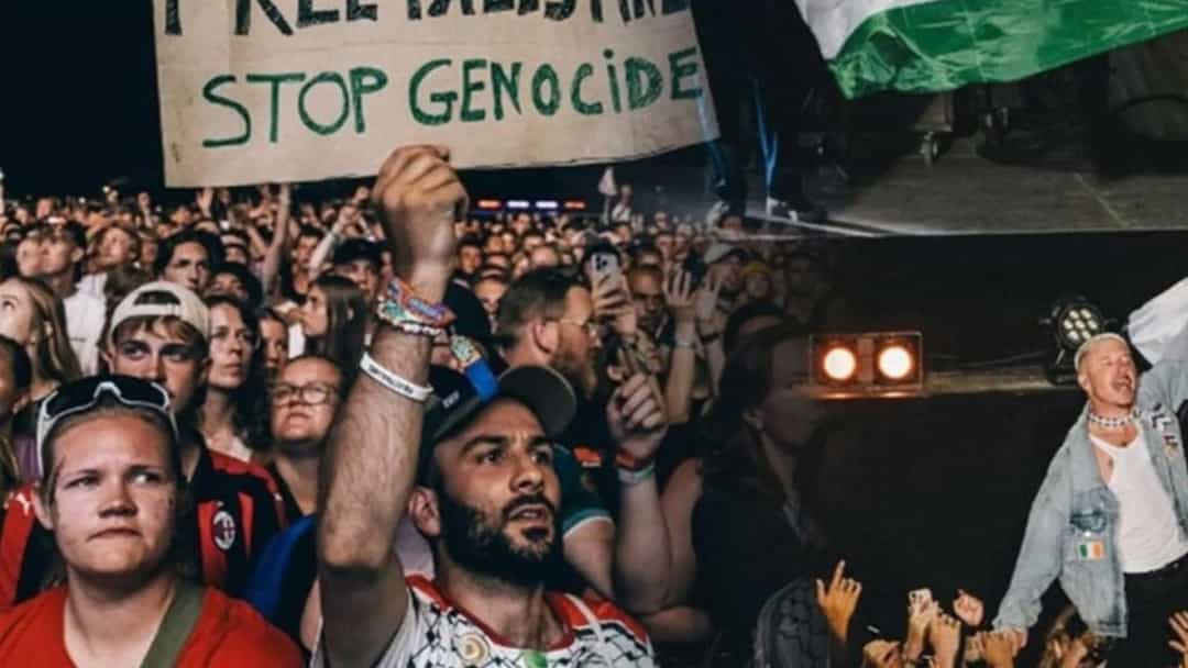 Macklemore, Filistin bayrağını kaldırarak konser sahnesinde kalabalığa sesleniyor.