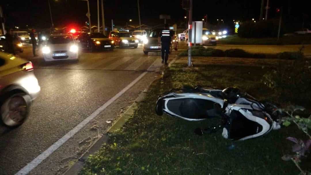 Gece saatlerinde yol kenarındaki çimenlik alanda devrilmiş bir motosiklet ve çevredeki trafik.