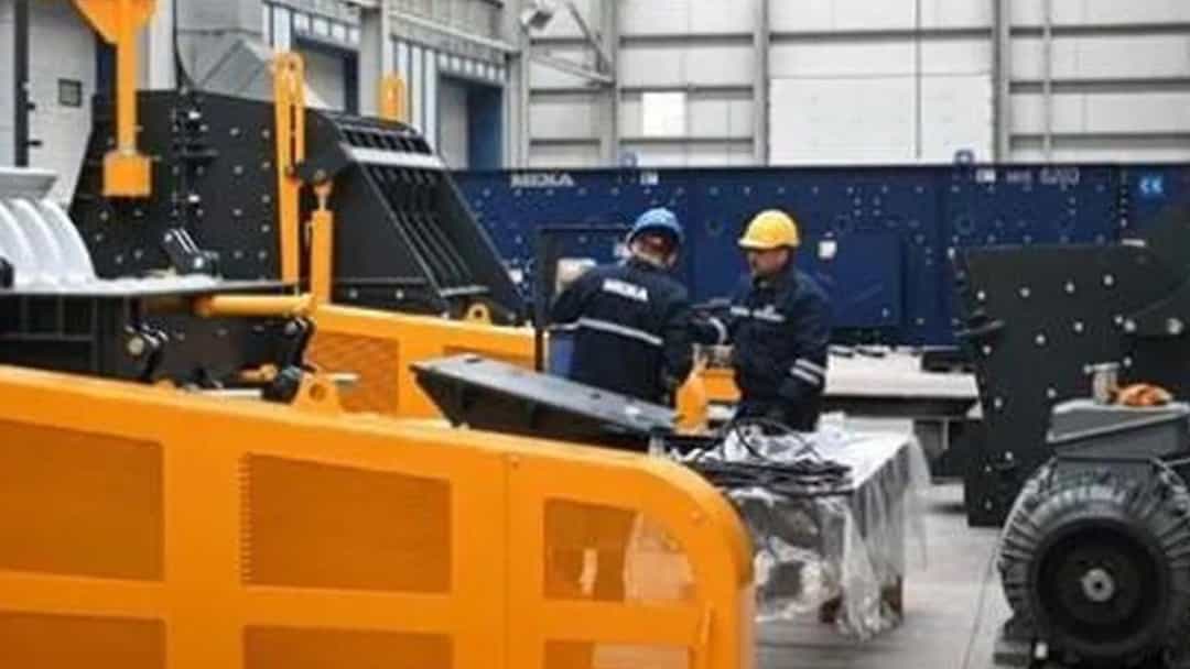 Bir atölyede ağır makinelerin yanında çalışan iki kişi