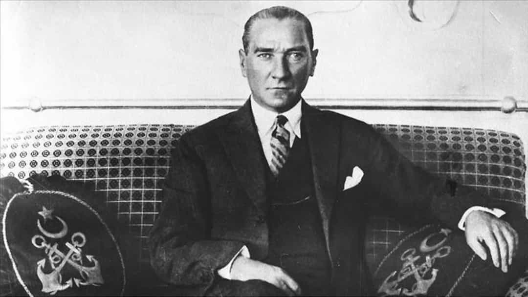 Mustafa Kemal Atatürk, desenli bir koltukta otururken çekilmiş siyah beyaz fotoğraf.