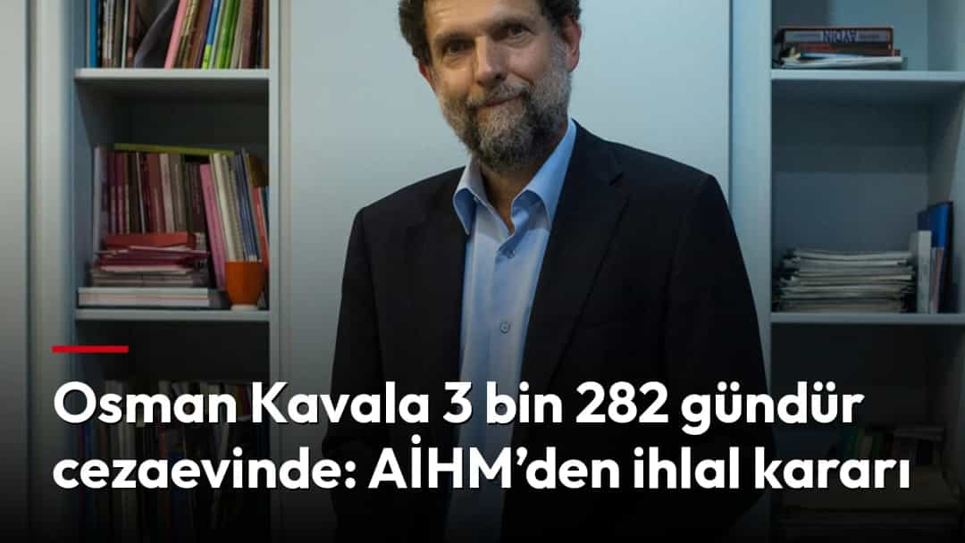 Osman Kavala, kitaplıkların bulunduğu bir odada ayakta duruyor.