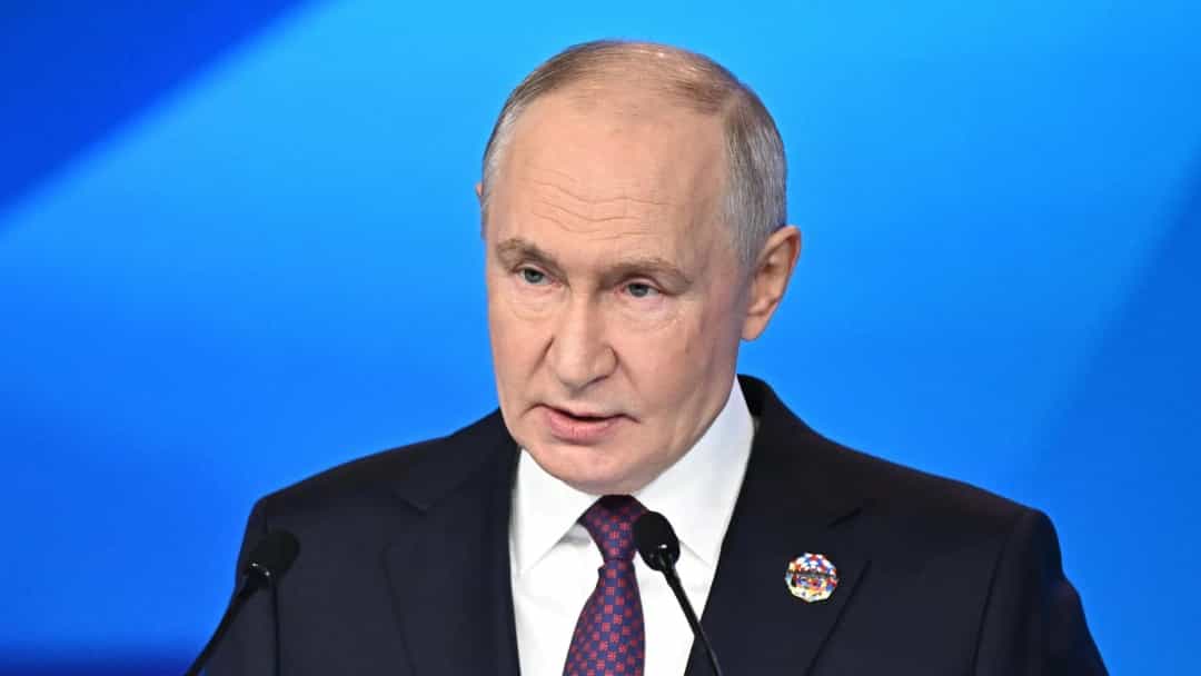 Vladimir Putin, mavi bir arka plan önünde kürsüde konuşurken.