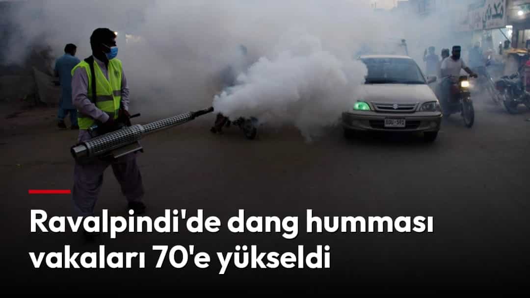 Koruyucu giysili bir görevli, araç ve motosikletlerin bulunduğu caddede dang humması sivrisineklerine karşı sisleme yapıyor.