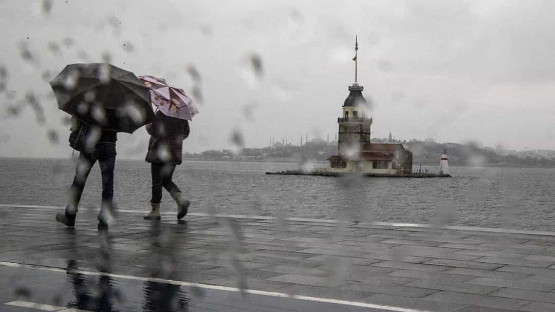 Yağmurlu havada şemsiye taşıyan yayalar, İstanbul’daki Kız Kulesi’nin önünden geçiyor.
