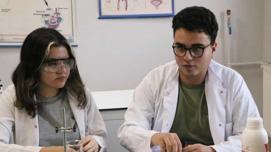 Laboratuvarda beyaz önlük giyen iki araştırmacı, deney malzemeleriyle çalışıyor.