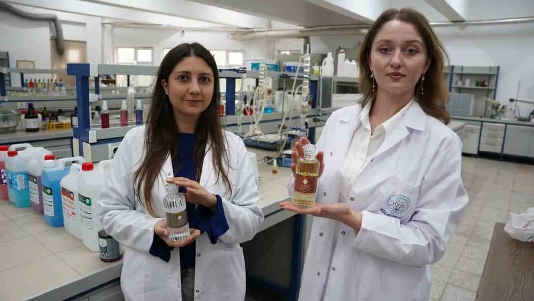 Laboratuvarda beyaz önlük giyen iki öğrenci, ürettikleri kolonyaları gösteriyor.