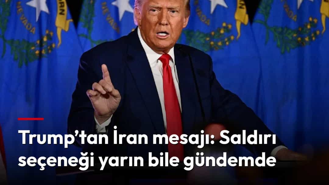 Donald Trump kürsüde konuşurken elini kaldırıyor; arka planda mavi bayraklar görülüyor.