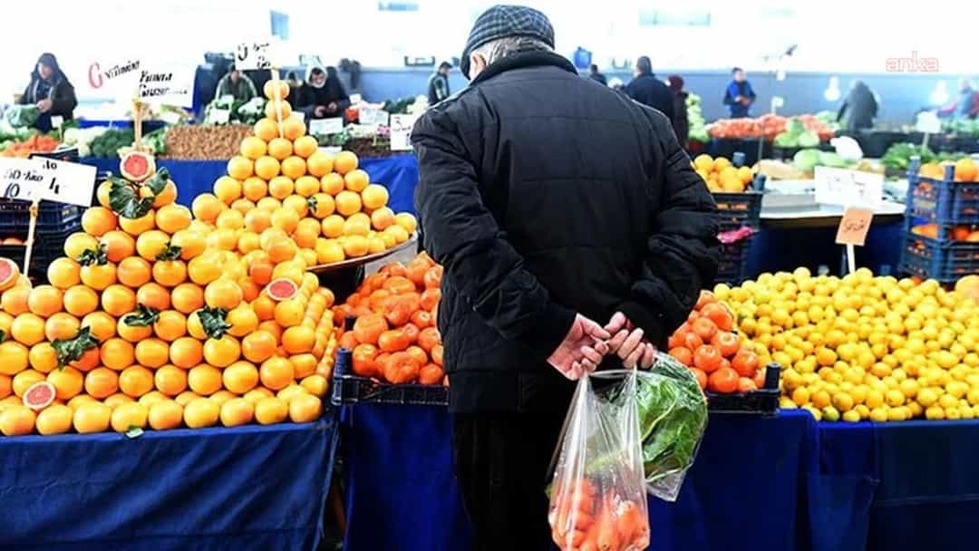 Bir kişi pazarda tezgâhlardaki portakal ve diğer meyvelerin önünde alışveriş yapıyor.