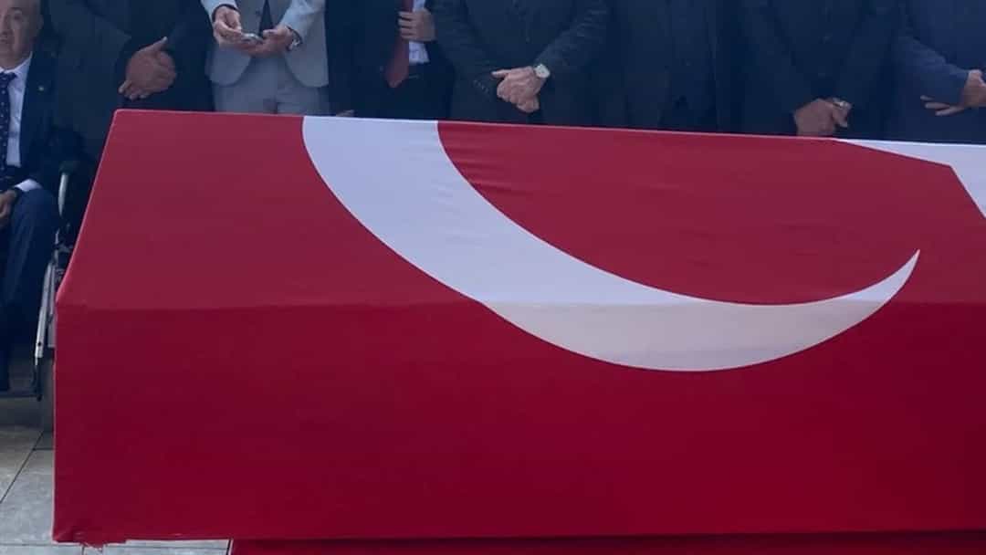 Türk bayrağına sarılı tabut, cenaze töreninde cami avlusunda bulunan kalabalığın önünde taşınıyor.