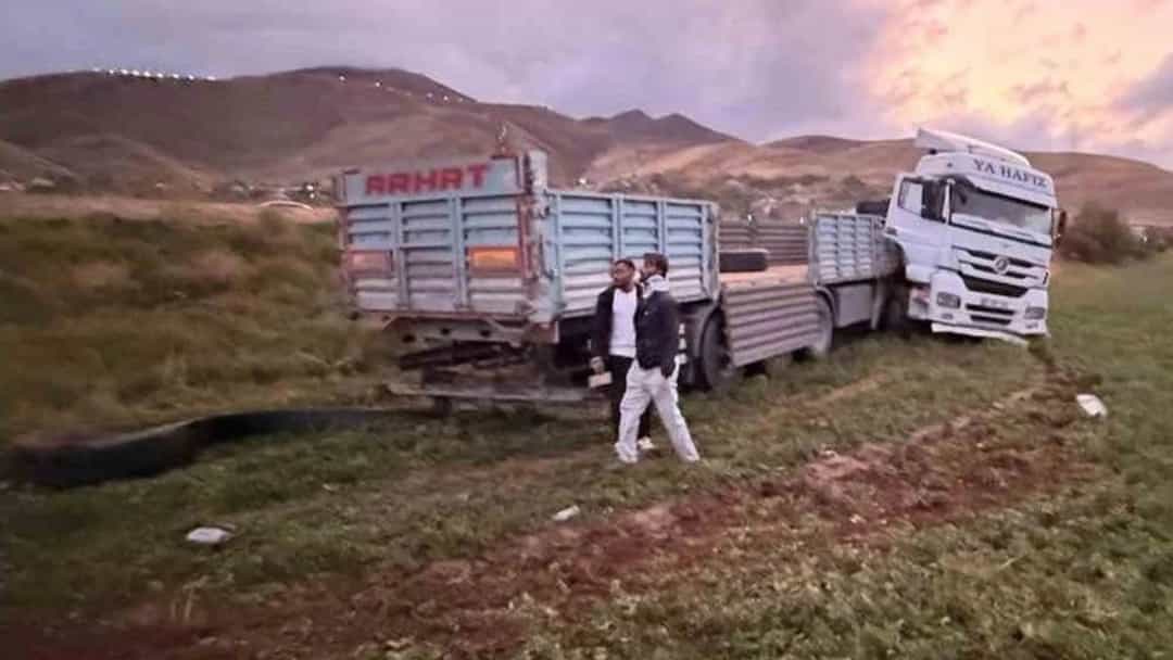 Kırsal bir arazide şarampole yuvarlanmış tır ve çevresinde duran kişiler.